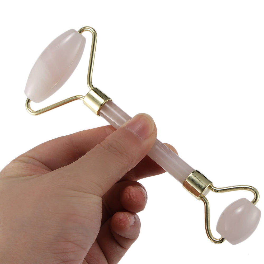 Hand holding a dual-ended pink stone facial roller with gold accents.
