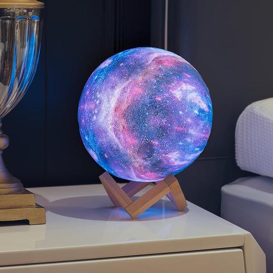 Glowing galaxy sphere lamp on a wooden stand, showing blue and pink nebula patterns.