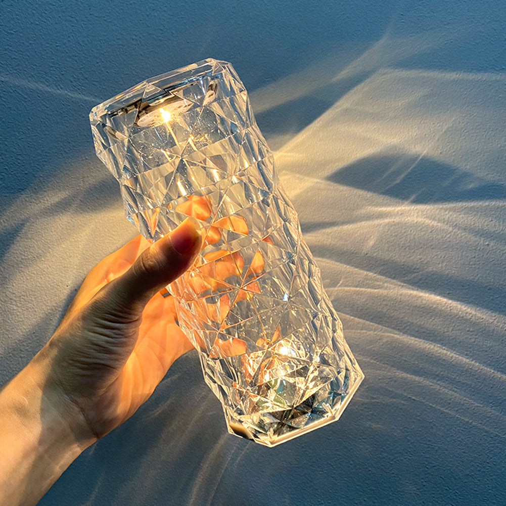 Hand holding a faceted crystal light with warm glow, casting geometric patterns on the wall.