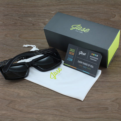 Black sunglasses, white pouch, and dark green box with lime text on a wooden surface.