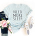 Light blue T-shirt with "Need More Sleep" text, paired with jeans, pink flowers, and white sneakers.