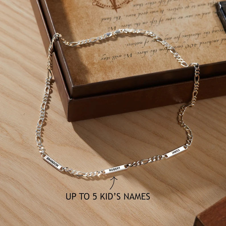 Silver chain bracelet with engraved names displayed on a brown box and wooden surface.
