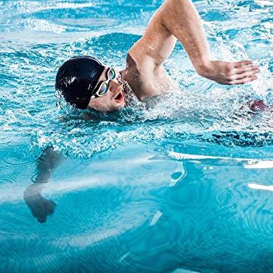 A swimmer in a black cap and goggles performs a freestyle stroke in a bright blue pool.