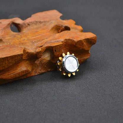 Gold gear-shaped button with silver center on textured wooden surface, gray background.