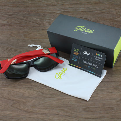 Red sunglasses, black lenses, gray box, and white pouch on wooden surface.