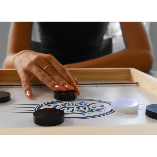 Hand playing a puck on a wooden tabletop game with black and white pieces.