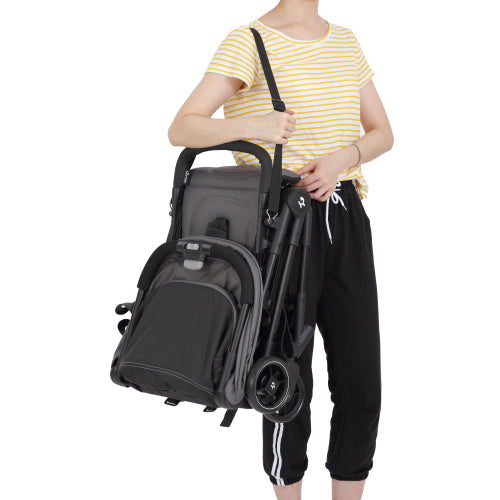 Woman holding a compact, folded black stroller with wheels, wearing a yellow striped shirt and black pants.