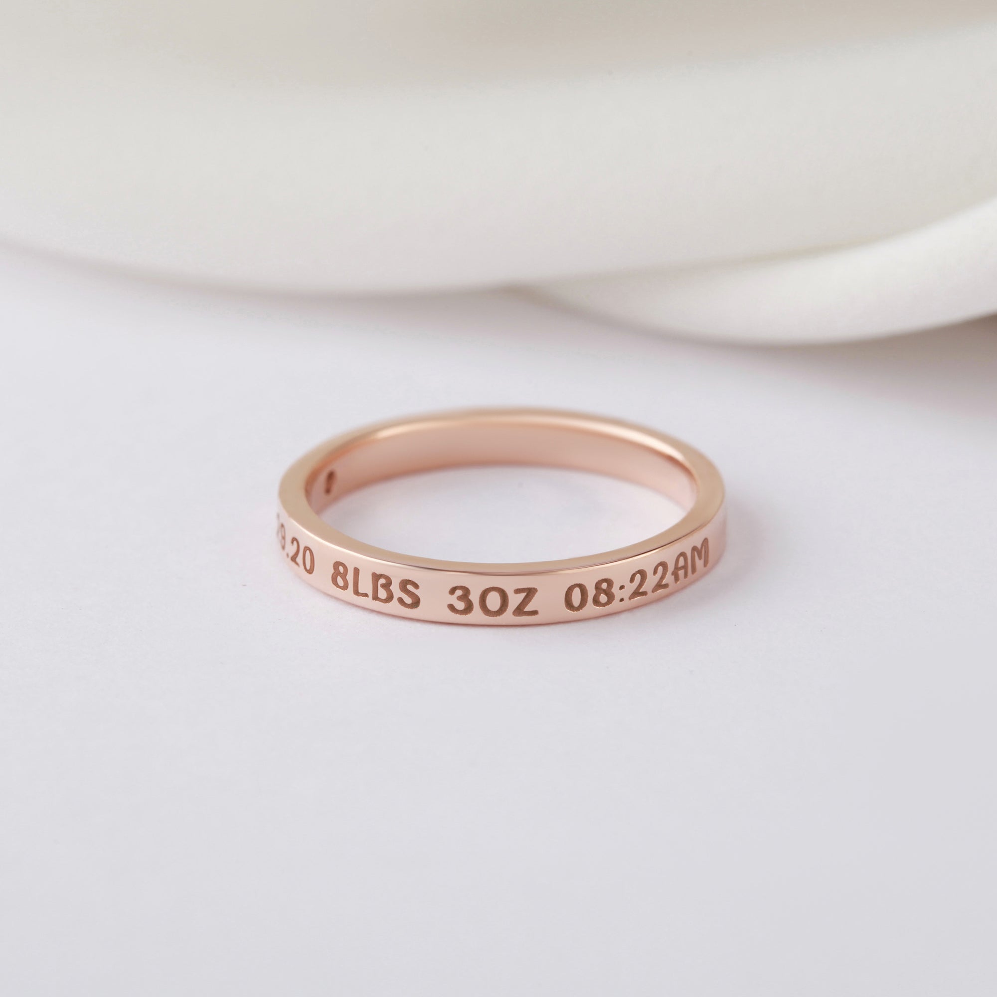 Rose gold ring on a white surface, engraved with date, weight, and time details.