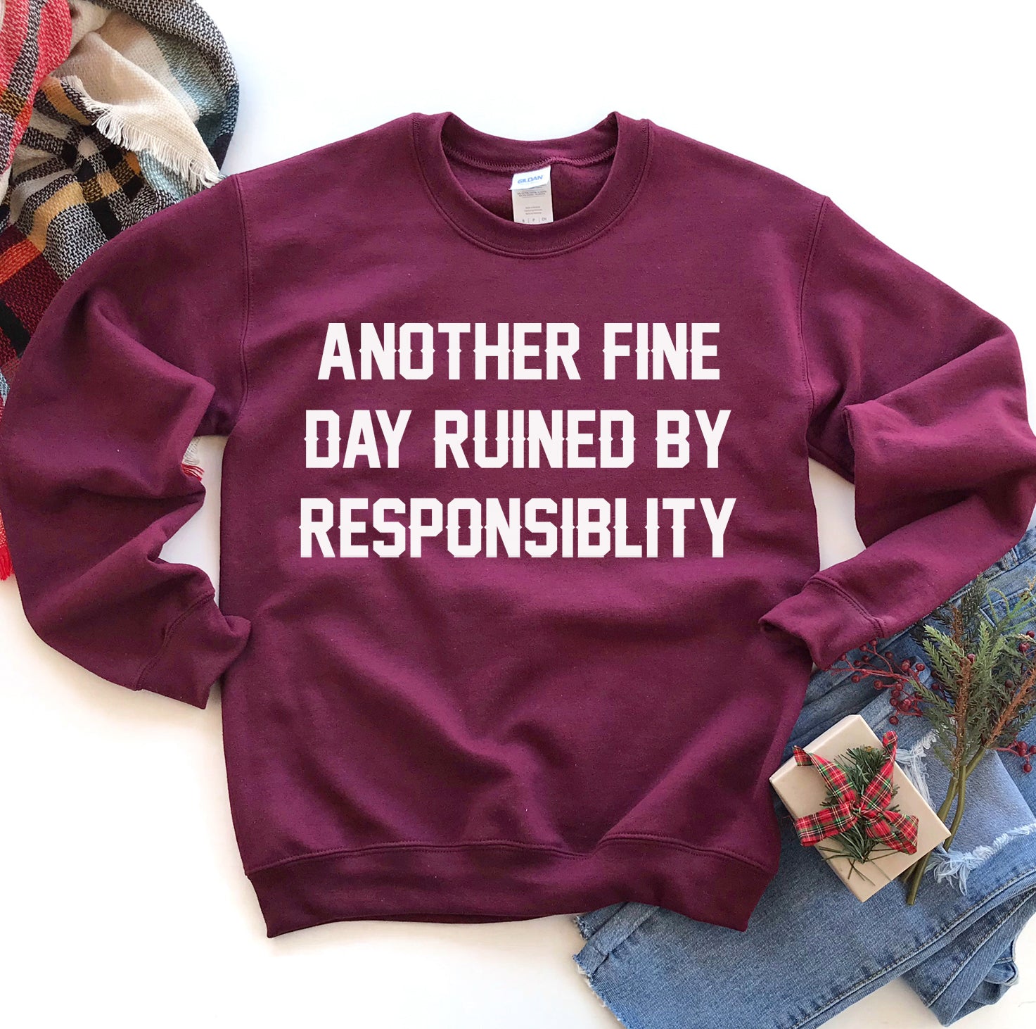 Maroon sweatshirt with white text, "Another fine day ruined by responsibility," on a white background.