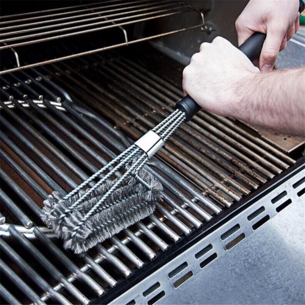 Hands using a bristle brush to clean a metallic grill grate.