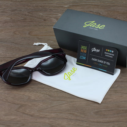 Sunglasses on a white pouch with a Jase box, business card, on a wood surface.