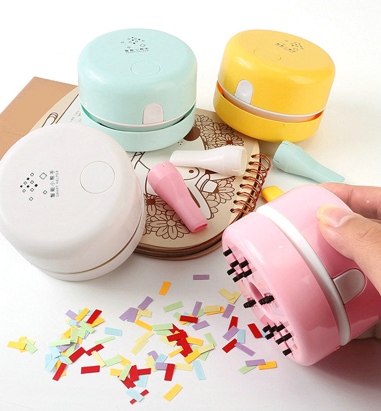 Colorful mini vacuums in pink, blue, yellow, and white on a notebook, with scattered confetti bits.