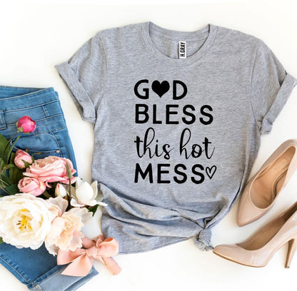 Gray t-shirt with "God bless this hot mess" text, next to pink heels, jeans, and flowers.