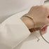 Hand wearing a gold bracelet with a dangling chain, against a white fabric background.