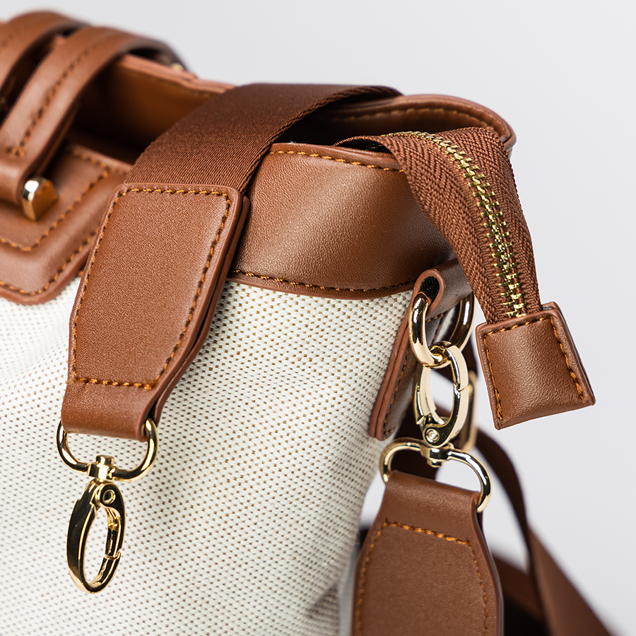 Brown leather-trimmed beige bag with gold clasps and zippers on a white background.