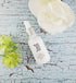 White dropper bottle with silver cap on cracked blue surface, surrounded by white and green flowers.