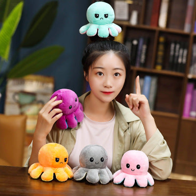 A woman poses with plush octopuses in vibrant colors: teal, purple, orange, gray, and pink.