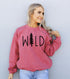 Woman in red "WILD" sweater with tree design, standing against a light gray wall.
