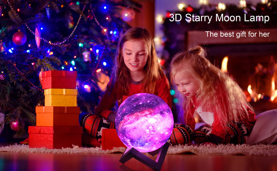 Two children in pajamas admire a glowing purple moon lamp near a Christmas tree and gifts.