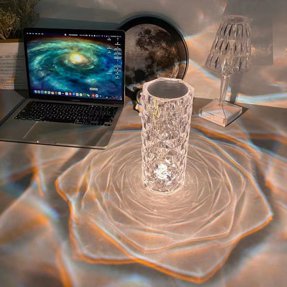 Crystal vase casting colorful patterns, next to a laptop with a galaxy wallpaper and a crystal lamp.