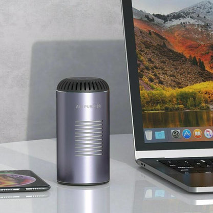 Silver air purifier next to a laptop displaying a mountain scene; phone on glossy table.