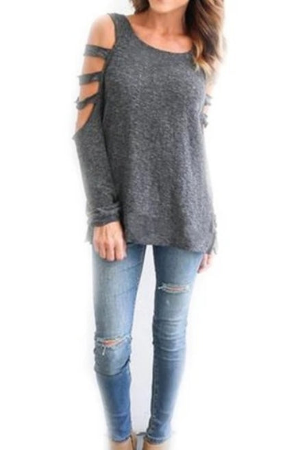 Woman in a grey cold-shoulder top and ripped blue jeans against a white background.