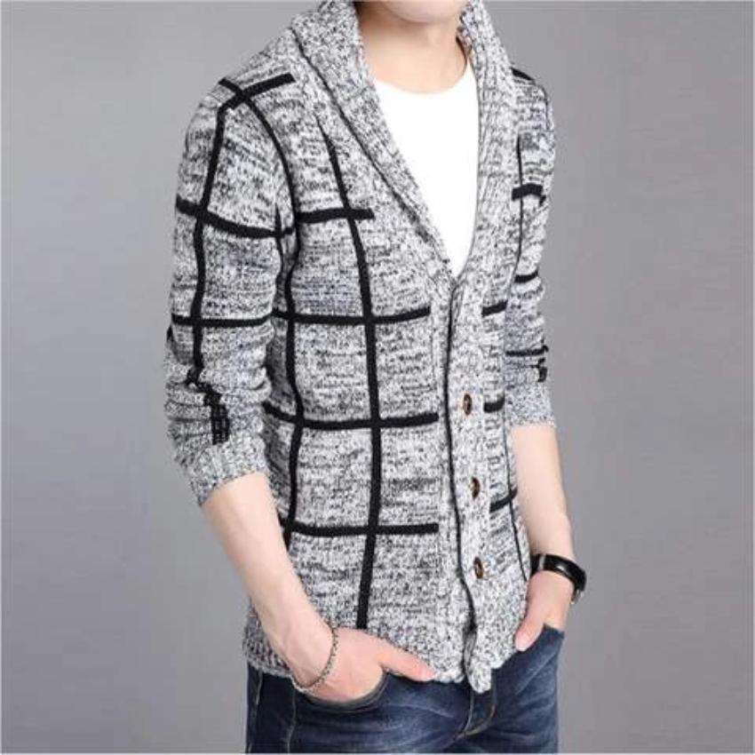 Person wearing a gray cardigan with a black grid pattern and brown buttons, hands in jeans pockets.
