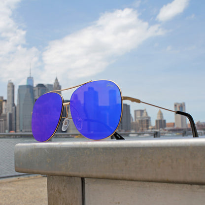 Blue-lensed aviator sunglasses on a ledge, with a city skyline and cloudy sky in the background.