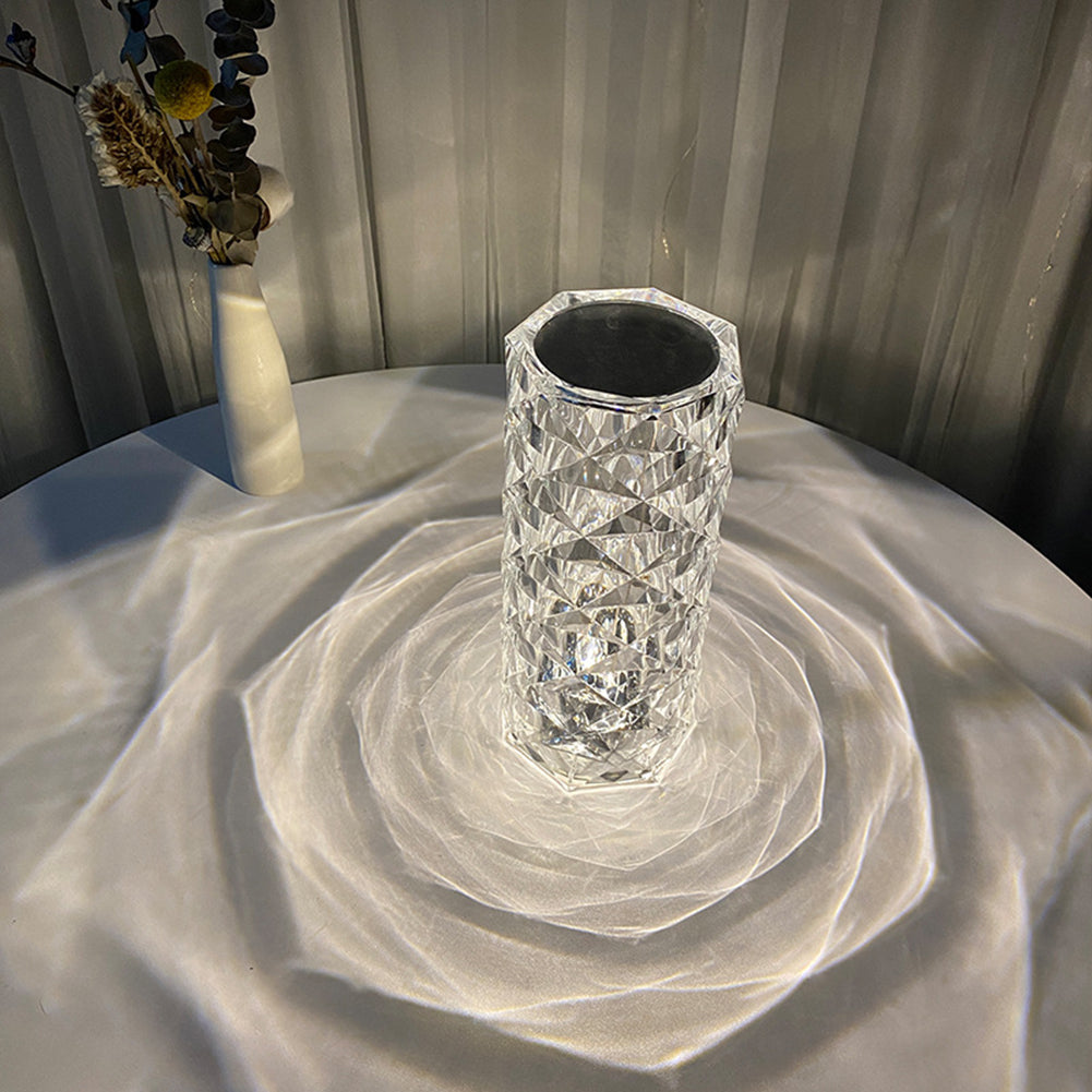 Crystal vase on a round table, casting geometric light patterns; dried flowers in the background.