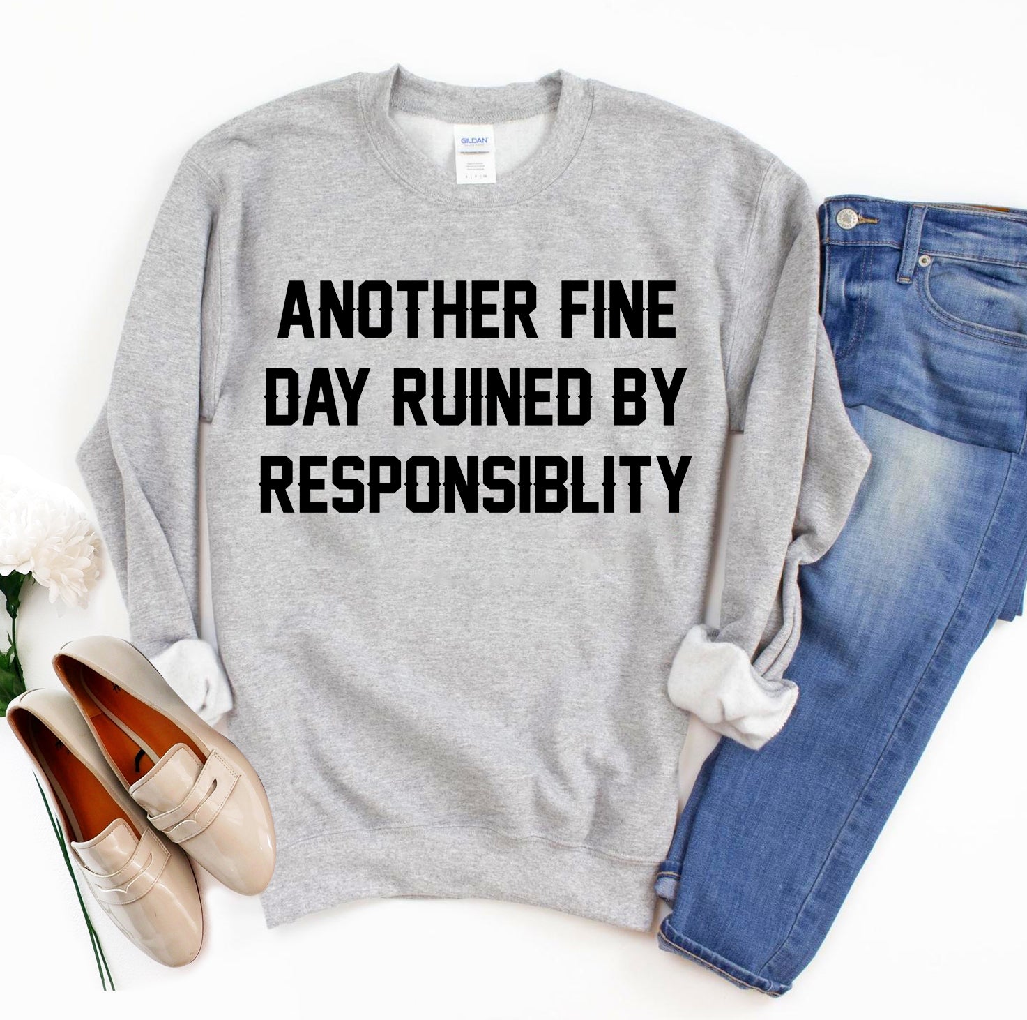 Gray sweatshirt with bold text, paired with blue jeans and beige loafers on a white background.