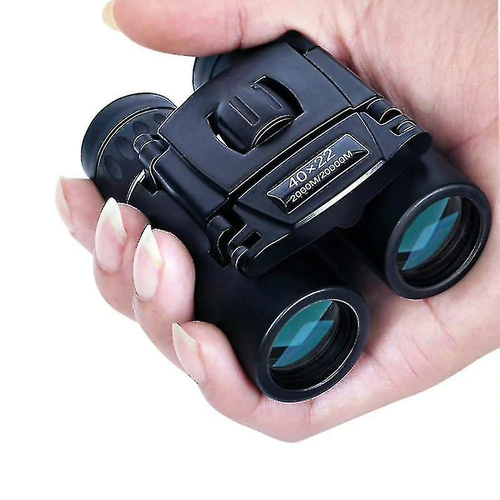Hand holding compact black binoculars with blue-tinted lenses and visible focus dial.