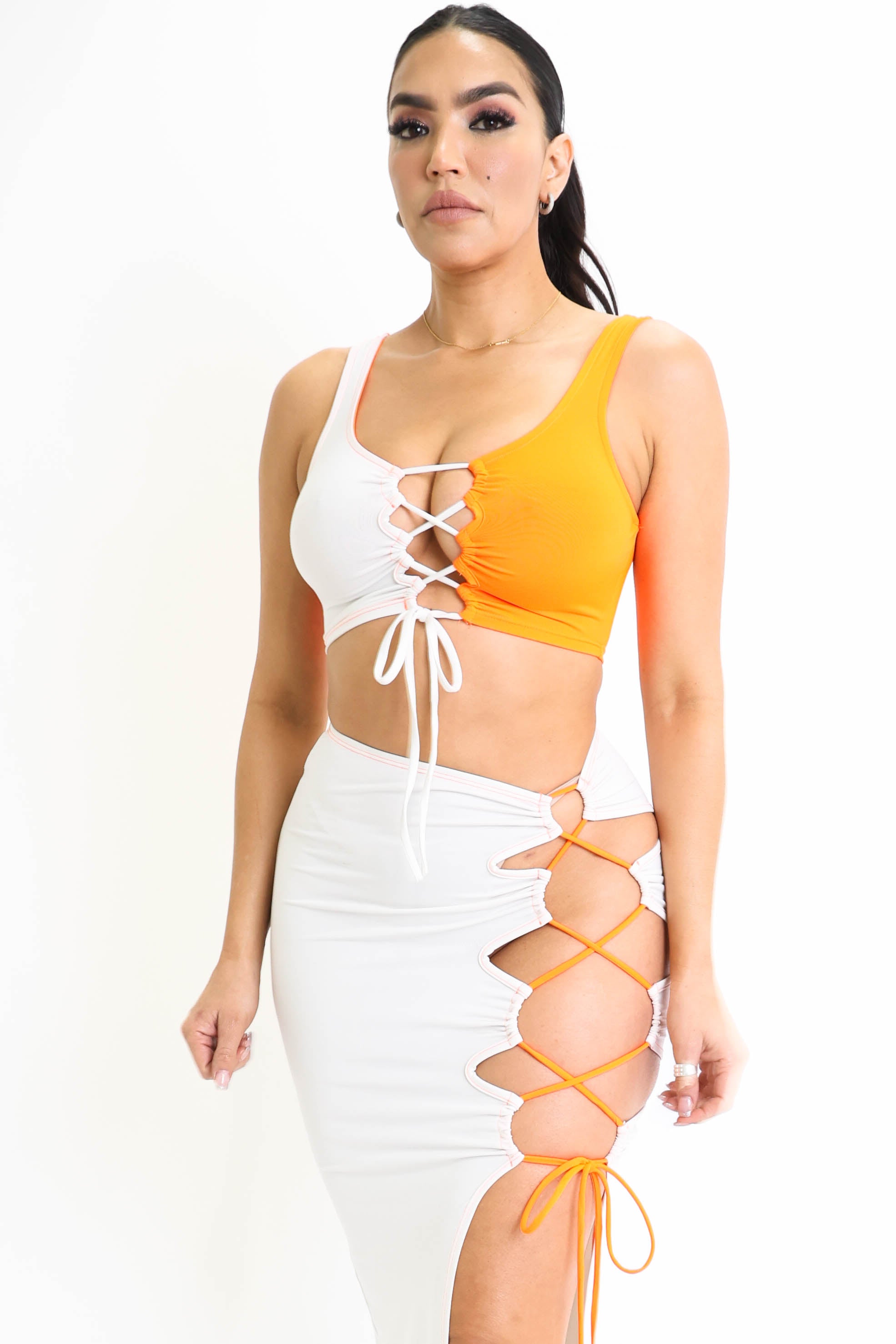 Woman in orange and white lace-up top and skirt with side cut-out design against a white backdrop.