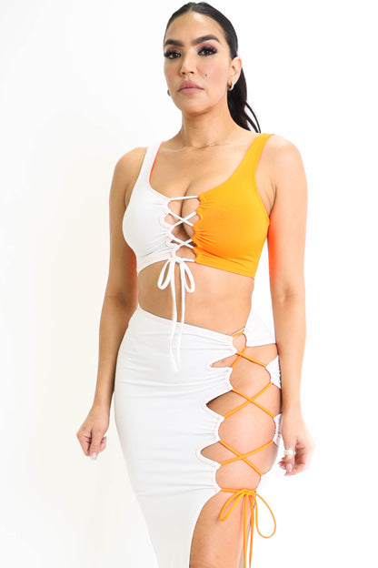 Woman in orange and white lace-up top and skirt with side cut-out design against a white backdrop.