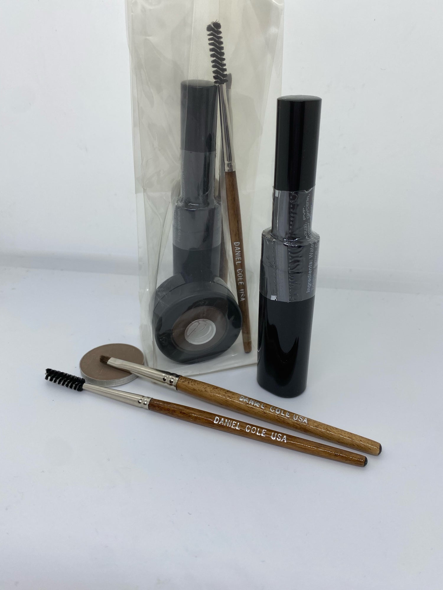 Makeup items with black tubes, two brown-handled brushes, and a round compact on a white background.