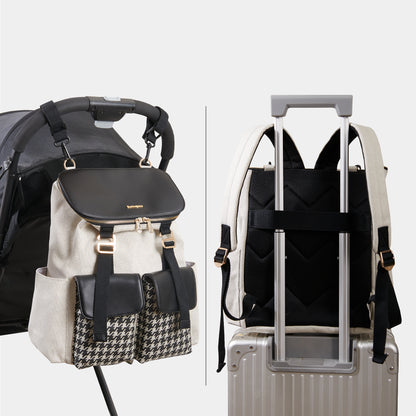 Cream and black backpack with houndstooth pockets on a stroller and suitcase handle.
