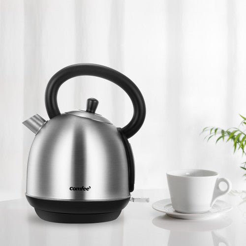 Stainless steel kettle with black handle beside a white teacup and saucer on a bright background.