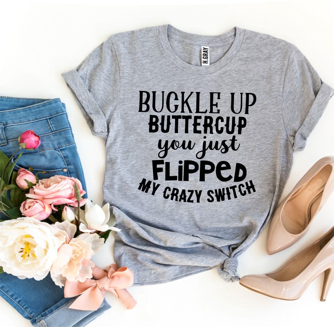Gray t-shirt with bold black text, jeans, pink and white flowers, and beige heels on a white surface.