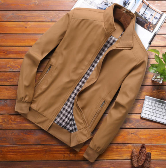 Tan jacket with plaid lining on wooden surface, beside a keyboard and plant.