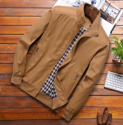 Tan jacket with plaid lining on wooden surface, beside a keyboard and plant.
