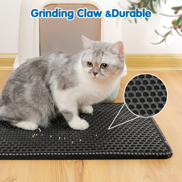 Gray and white cat on black textured mat with paw print pattern near litter box.