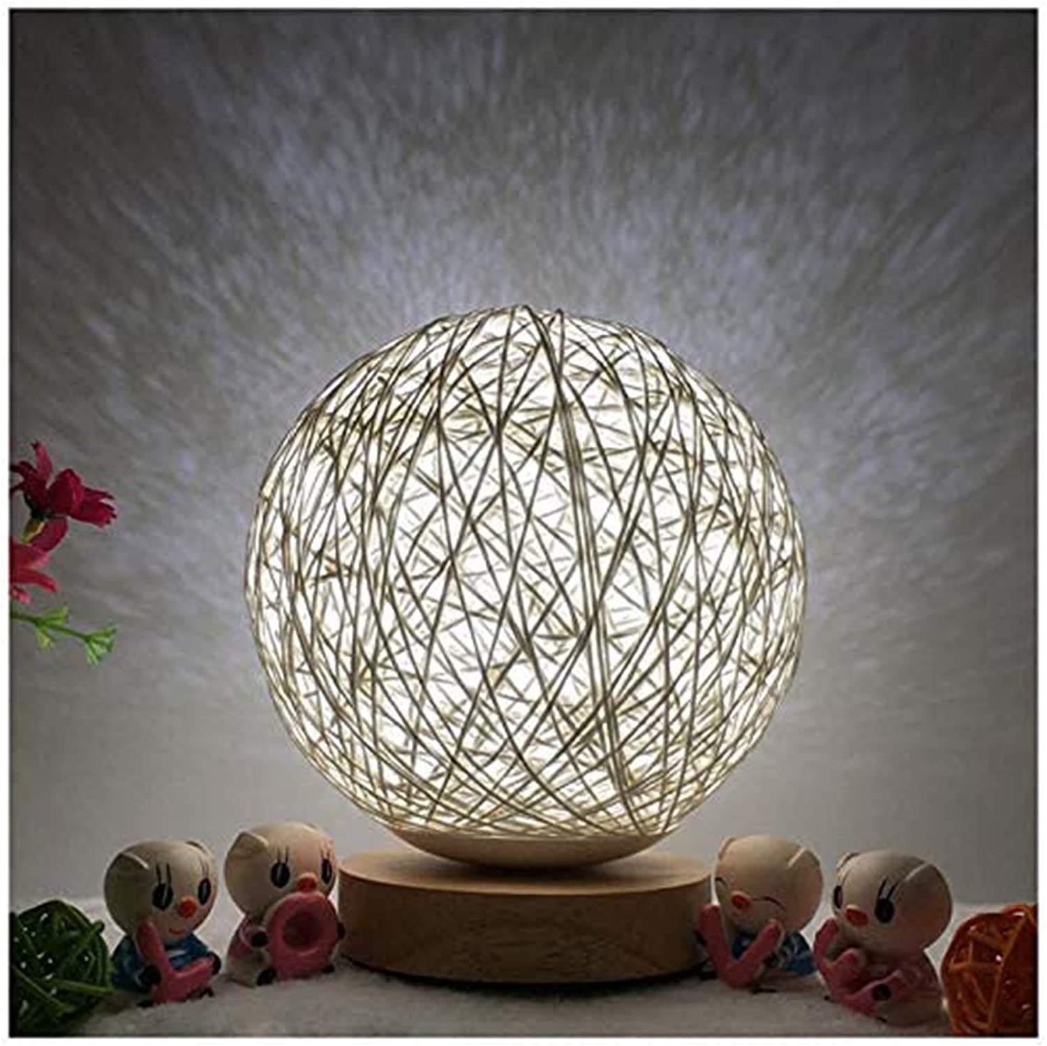 A glowing spherical string lamp on a wooden base, surrounded by small colorful figurines.