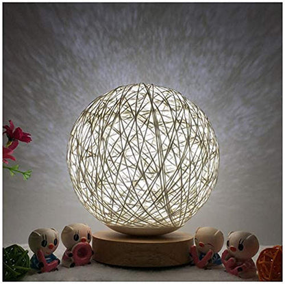 A glowing spherical string lamp on a wooden base, surrounded by small colorful figurines.