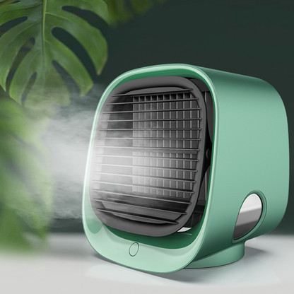 A green portable fan emitting mist, set against a backdrop of blurred green leaves.