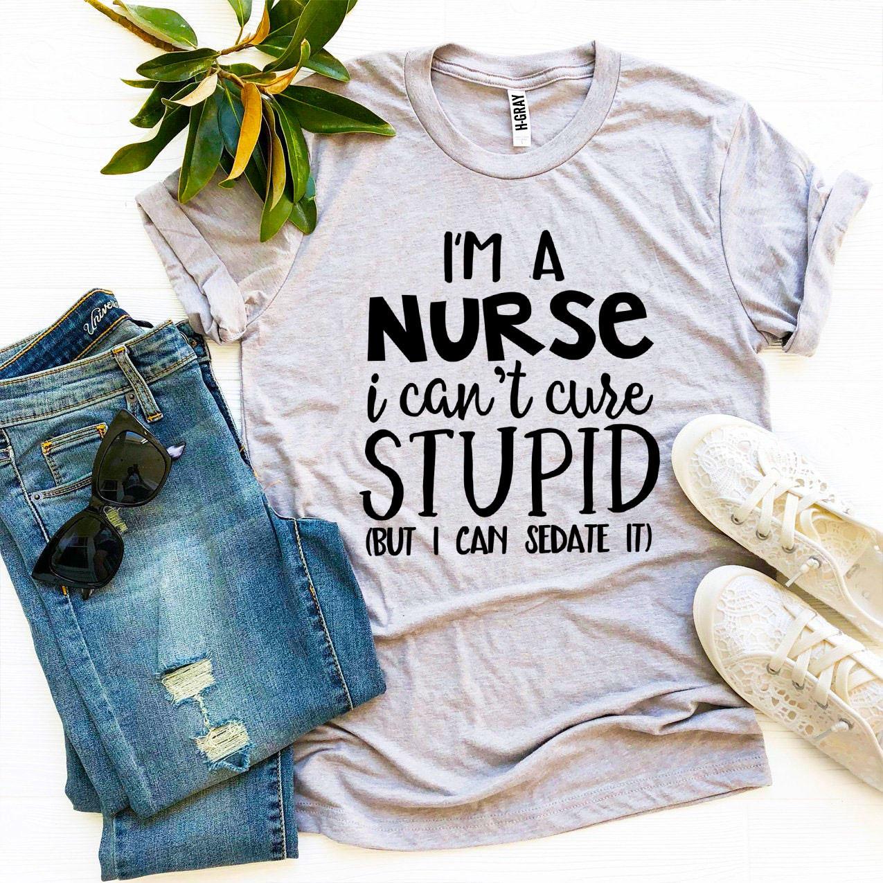 Gray T-shirt with bold black text, blue jeans, sunglasses, white shoes, and green leaves nearby.