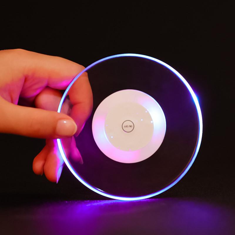 Hand holding a glowing circular disc with purple and blue LED lights on a dark background.