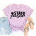 Pink T-shirt with "Stay Pawsitive" in black, ripped denim shorts, and beige sandals.