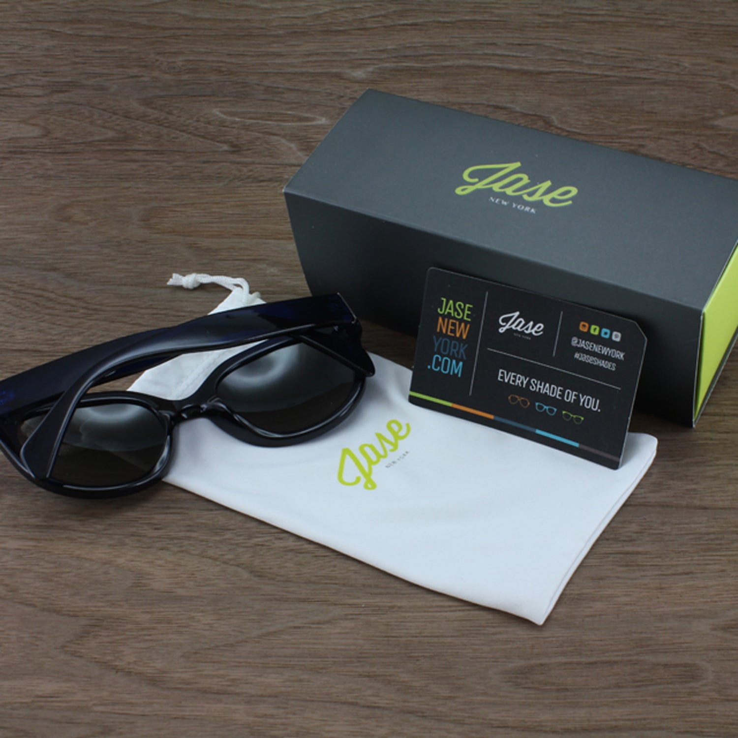Sunglasses on white pouch, black card, and black box with green logo on wood surface.