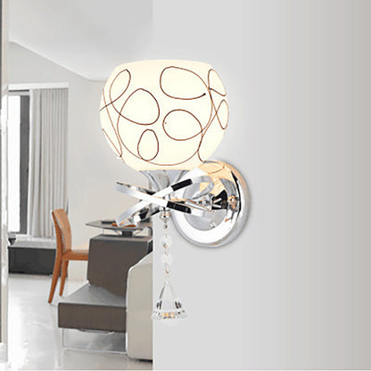 Modern wall lamp with a patterned white shade, chrome fittings, and crystal pendant, in a bright room.