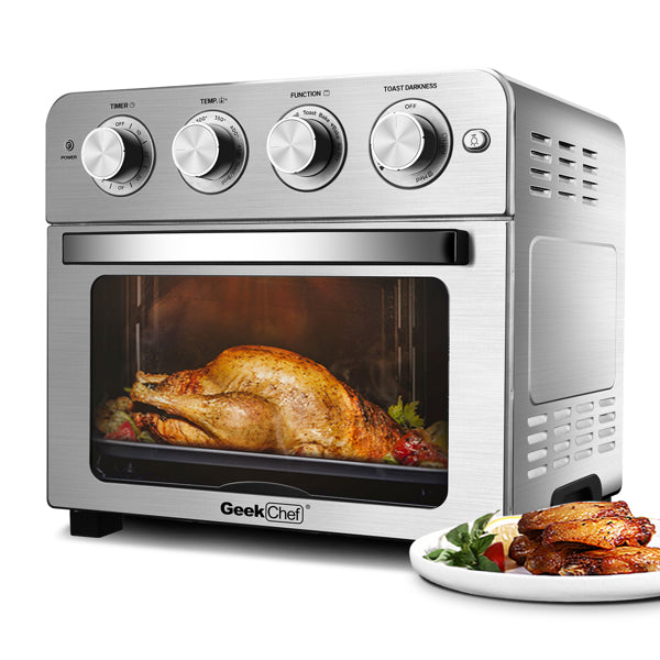 Silver oven with four dials, a roasting chicken inside, and a plate of cooked meat beside it.