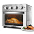 Silver oven with four dials, a roasting chicken inside, and a plate of cooked meat beside it.